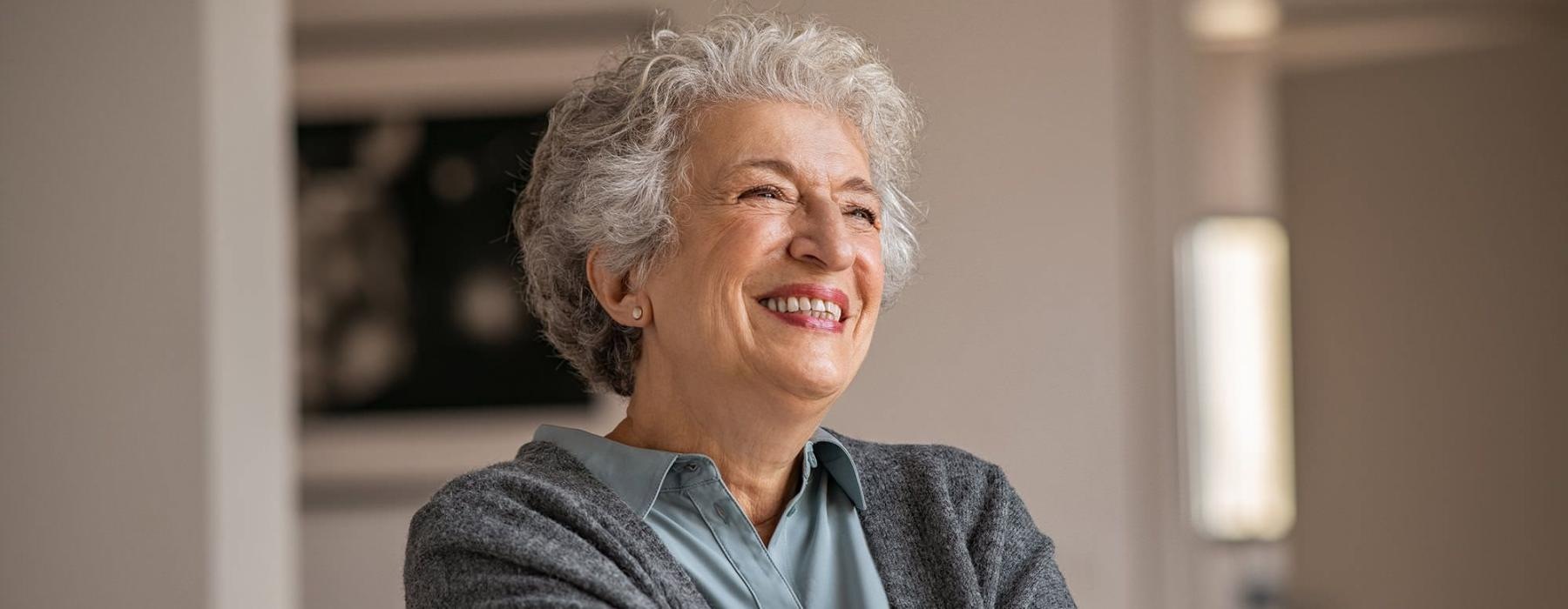 elderly woman with a cane, sits in a room and smiles